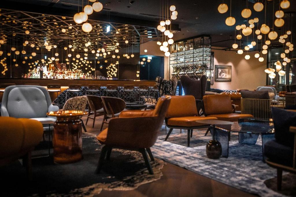Lounge e bar de hotel sofisticado com poltronas de couro marrom, iluminação pendente circular e atmosfera acolhedora à noite em Hamburgo.