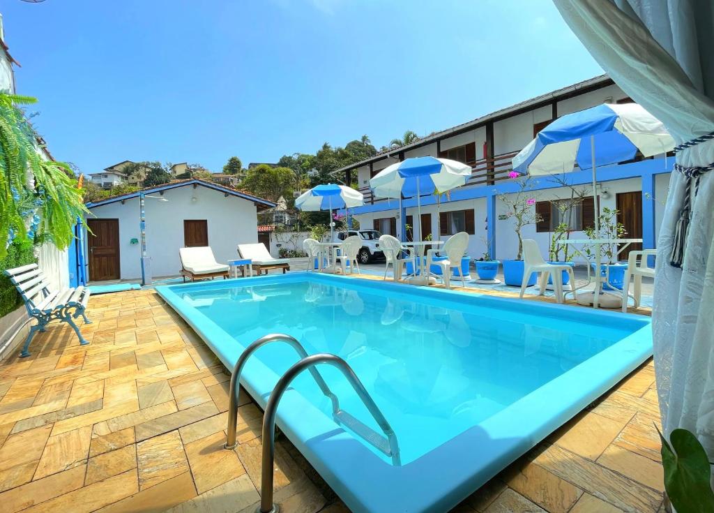 Piscina da Pousada Suítes Nova Mar Ilhabela, cercada por quartos, mesas e guarda-sóis azuis e brancos.