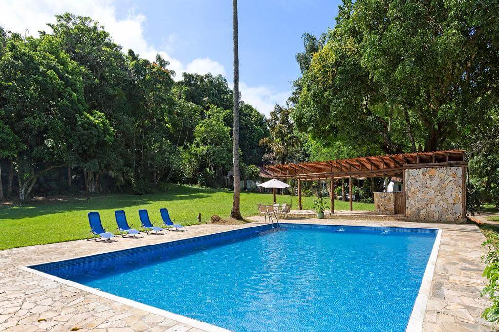 Piscina do Vila Siriúba Hotel, em Ilhabela, cercada por gramado, árvores e espreguiçadeiras.