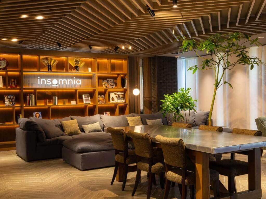 Área comum do insomnia KYOTO OIKE, em Kyoto, com sofá, mesa compartilhada, estantes iluminadas e plantas.