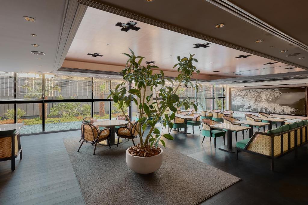 Área comum do Kyoto Century Hotel, em Kyoto, com mesas, poltronas, plantas e grandes janelas voltadas para o jardim.