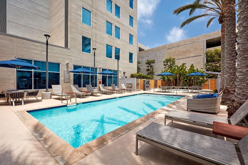 Piscina externa do Hyatt Place Los Angeles LAX El Segundo com espreguiçadeiras, guarda-sóis azuis e palmeiras