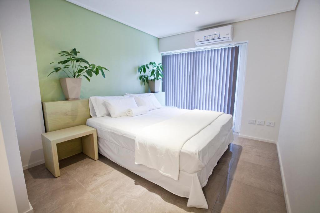 Quarto de casal minimalista no Le Montreal Apartments em Mendoza, com parede verde-claro, cama branca e vasos de plantas.