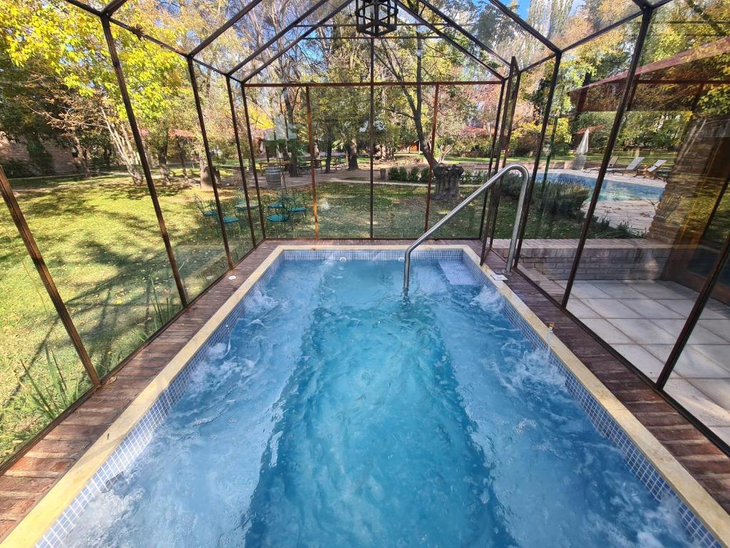 Piscina de hidromassagem coberta por estrutura de vidro no Luján de Cuyo B&B em Mendoza, cercada por árvores de outono.
