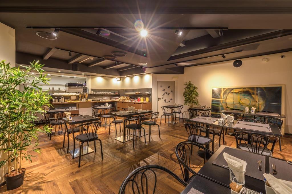 Sala de café da manhã do Hotel Roxy, em Milão, com mesas pretas, buffet ao fundo e piso de madeira