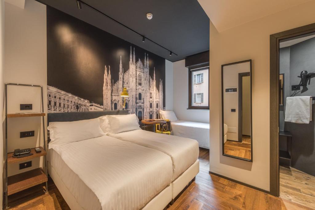 Quarto do Hotel Roxy, em Milão, com duas camas, parede decorada com imagem da Catedral de Milão e banheiro ao lado