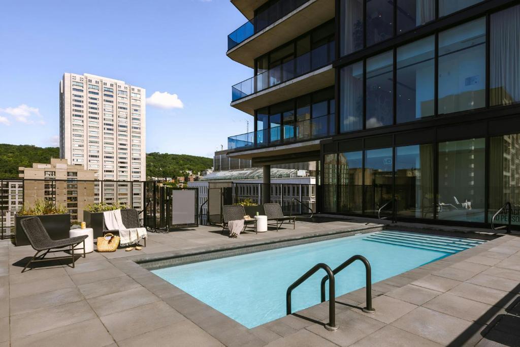 Piscina externa do Hotel Monville Downtown Montreal, em Montreal, cercada por espreguiçadeiras e edifícios.