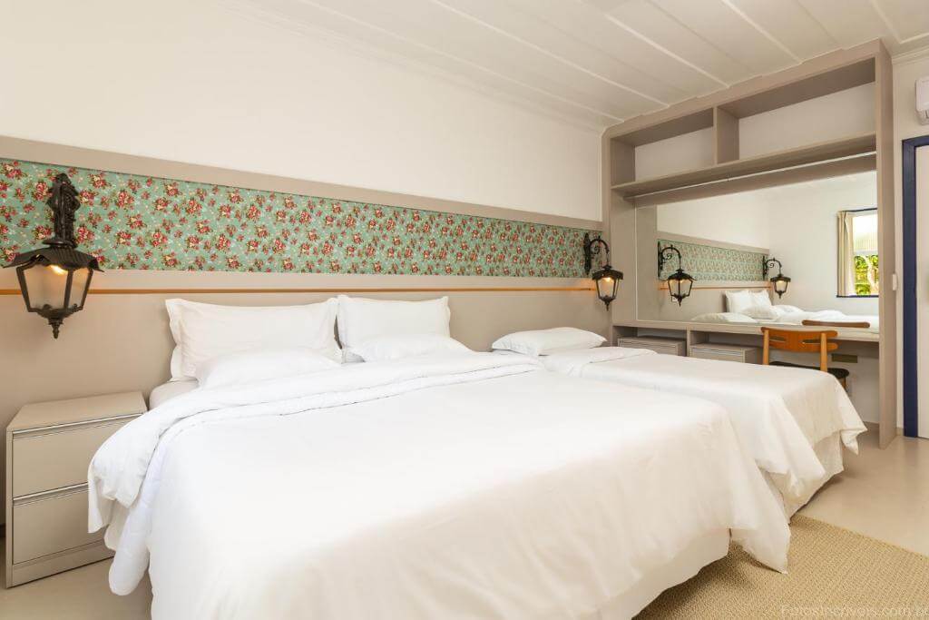 Quarto da Pousada Aconchego, em Paraty, com duas camas, decoração floral e espelho amplo.