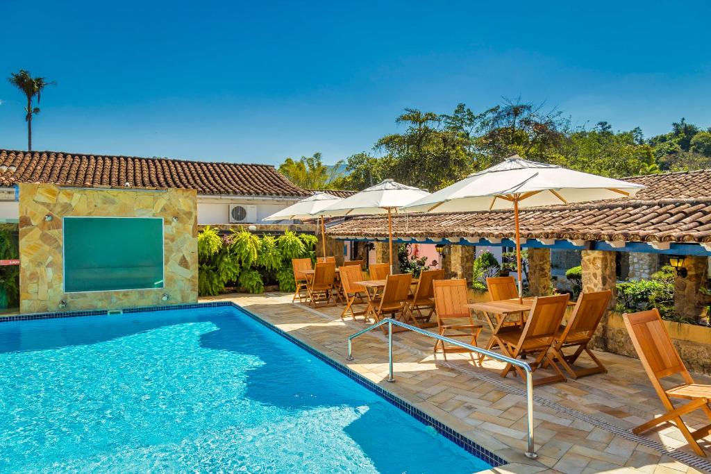 Piscina da Pousada Aconchego, em Paraty, com mesas, cadeiras de madeira e guarda-sóis.