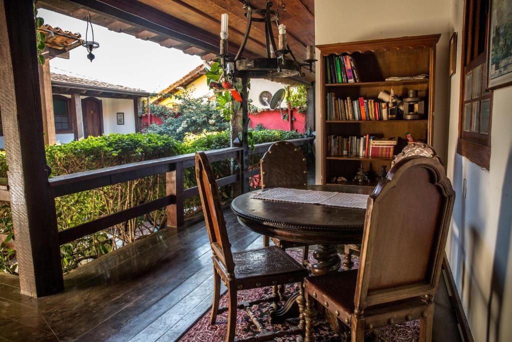 Varanda da Pousada Marendaz, em Paraty, com mesa de madeira, cadeiras antigas e estante de livros.