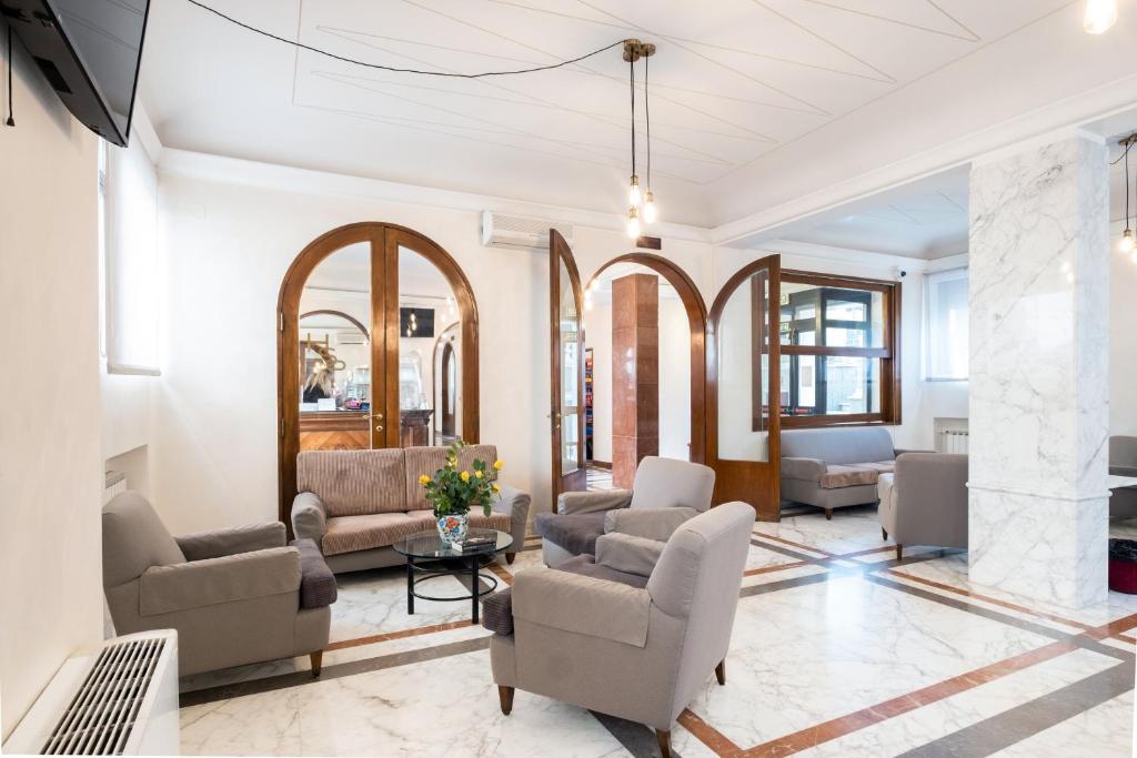 Sala de estar do Hotel Santa Prisca, em Roma, com poltronas, sofá e portas de madeira em arco.