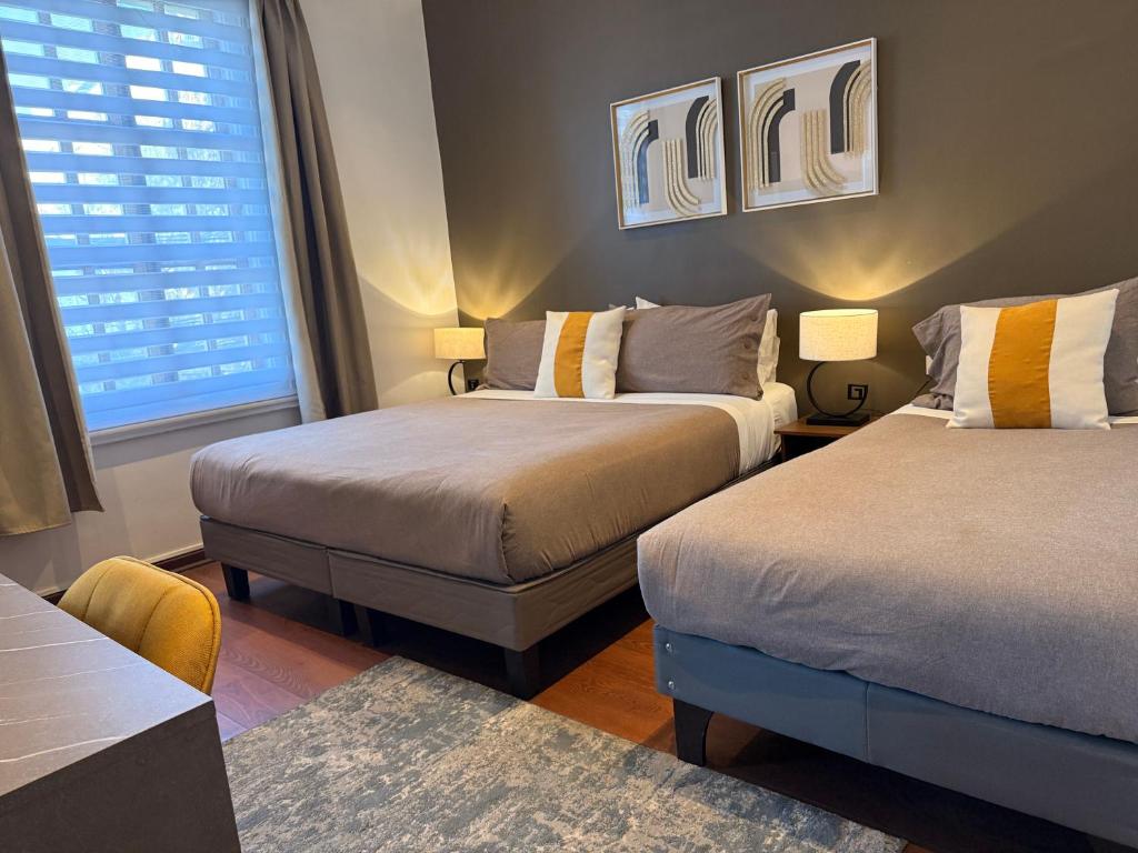 Quarto do H Ocoranza com duas camas de casal, roupa de cama cinza e detalhes mostarda, quadros abstratos e luminárias de mesa.