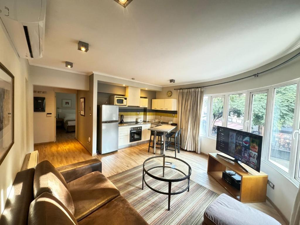 Sala e cozinha integradas do Lastarria Aparts com sofá de couro marrom, mesa de centro, cozinha equipada e janelas amplas.