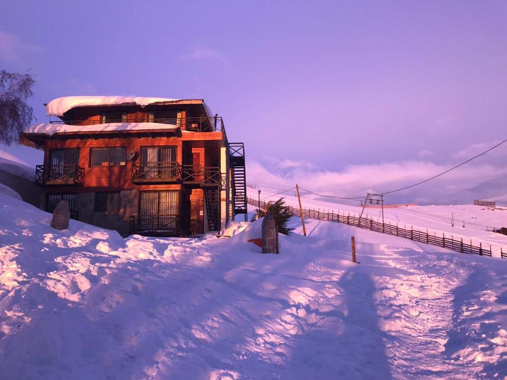 Fachada externa do Montaña Blanca coberta de neve, com varandas de madeira e vista da estação de esqui ao entardecer.