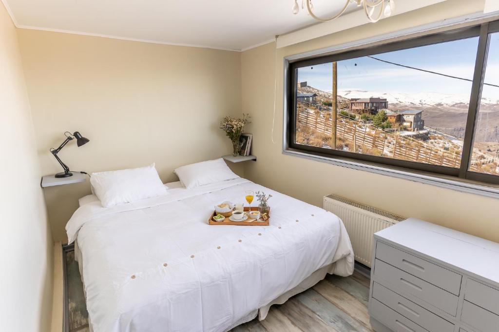 Quarto do Montaña Blanca com cama de casal, bandeja de café da manhã e janela panorâmica com vista da cordilheira nevada.