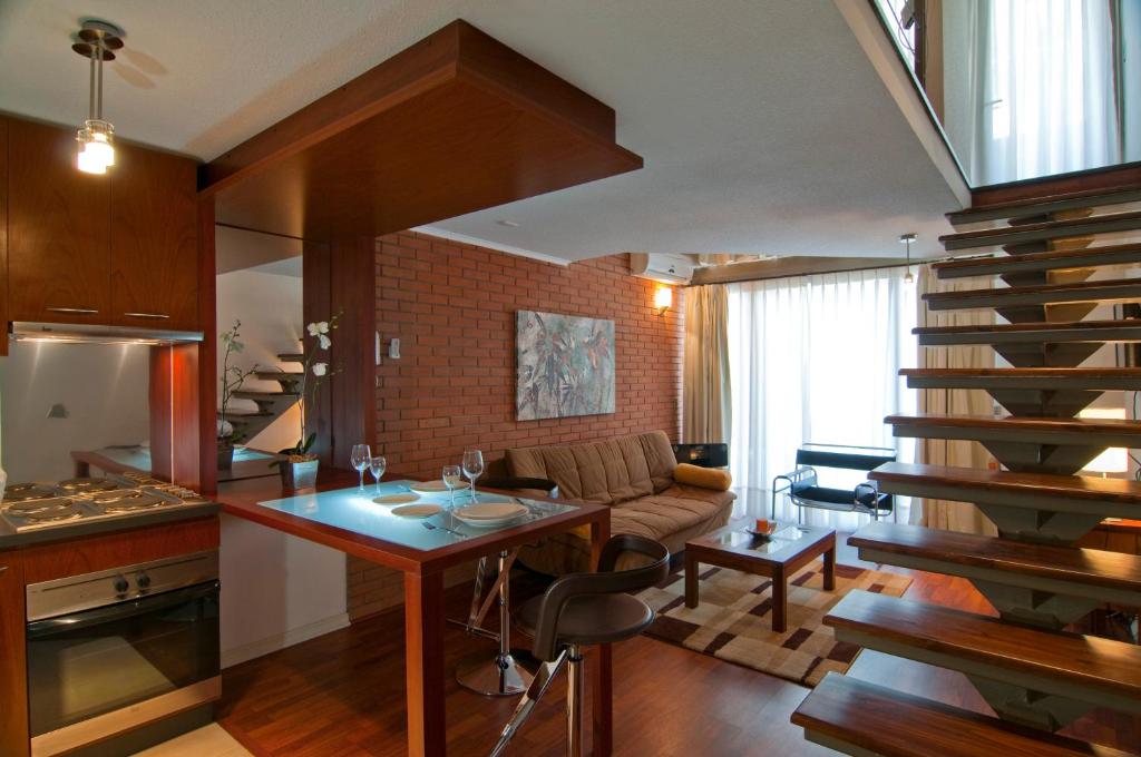 Apartamento duplex do Park Plaza Apart Hotel com cozinha compacta, mesa de jantar, sofá e escada de madeira suspensa.