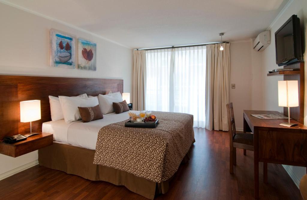 Quarto do Park Plaza Apart Hotel com cama de casal, bandeja de café da manhã, escrivaninha de madeira e cortinas brancas.