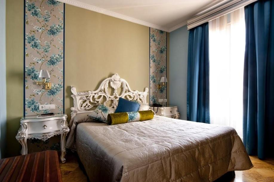 Quarto de hotel elegante com cabeceira entalhada e cortinas azuis no Adriano Boutique Sevilla em Sevilha.