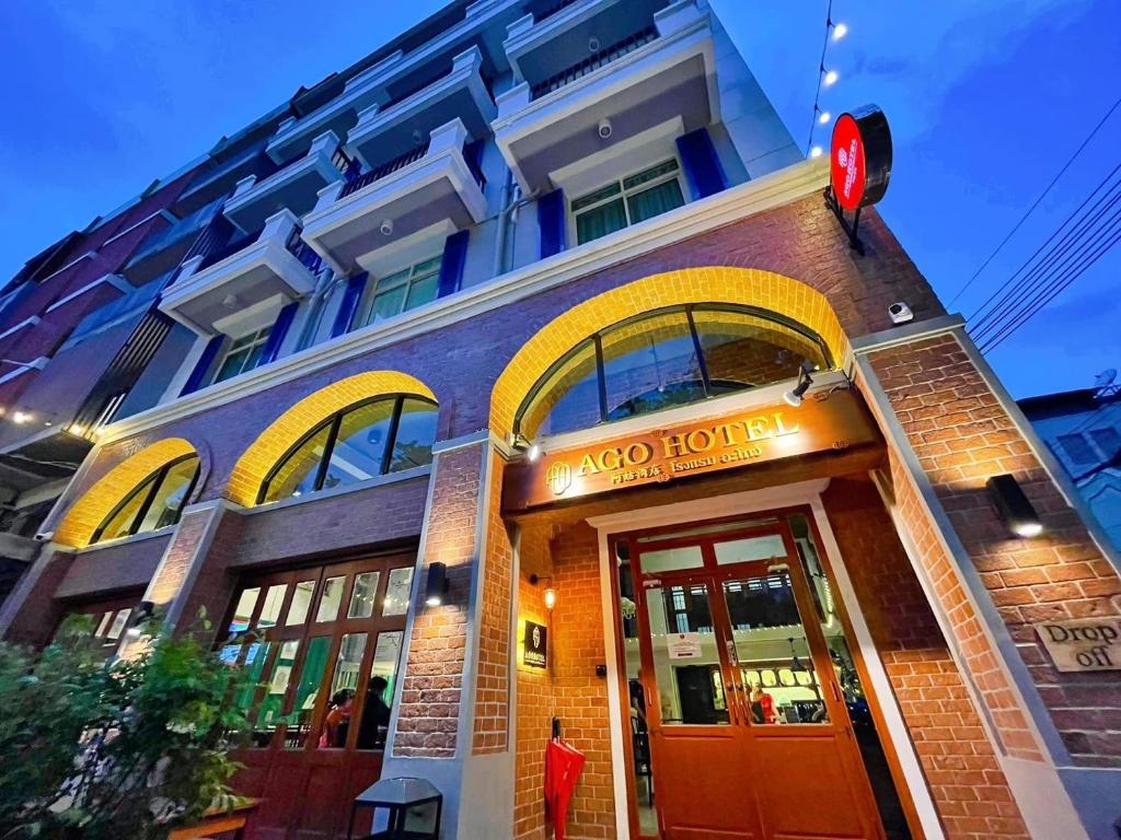 Fachada exterior do AGO HOTEL à noite com fachada de tijolos vermelhos, janelas em arco iluminadas e varandas azuis nos pisos superiores.