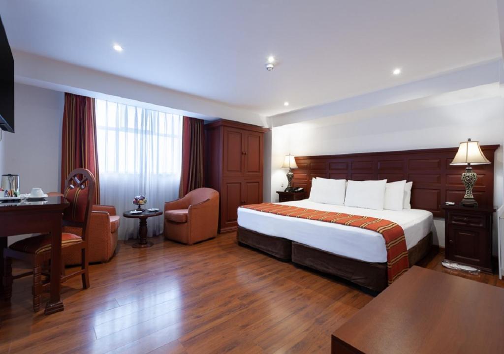 Quarto do Terra Andina Colonial Mansion com cama de casal ampla, cabeceira em madeira escura, estação de trabalho e duas poltronas junto à janela.